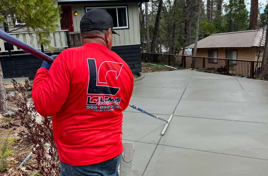 A professional crew member from Lemus Concrete LLC, wearing a branded company shirt with their C-8 license number, uses a bull float to apply a smooth, clean finish to a newly poured residential concrete patio.