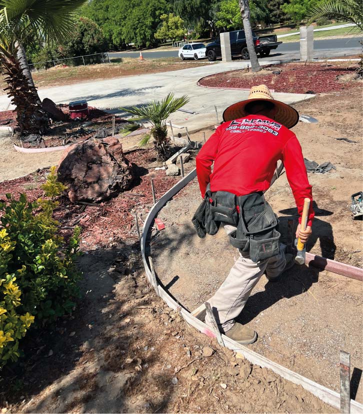 Professional concrete contractor from Lemus Concrete LLC wearing a branded red work shirt while setting wooden forms for a curved residential concrete walkway in Fresno, CA